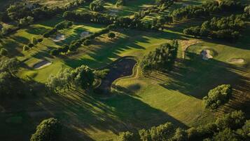 An aerial view of a golf course with multiple holes, trees, and a small pond.