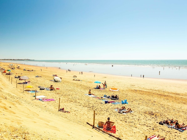 Ein Strand mit badenden Personen, Sonnenschirmen und Liegestühlen.