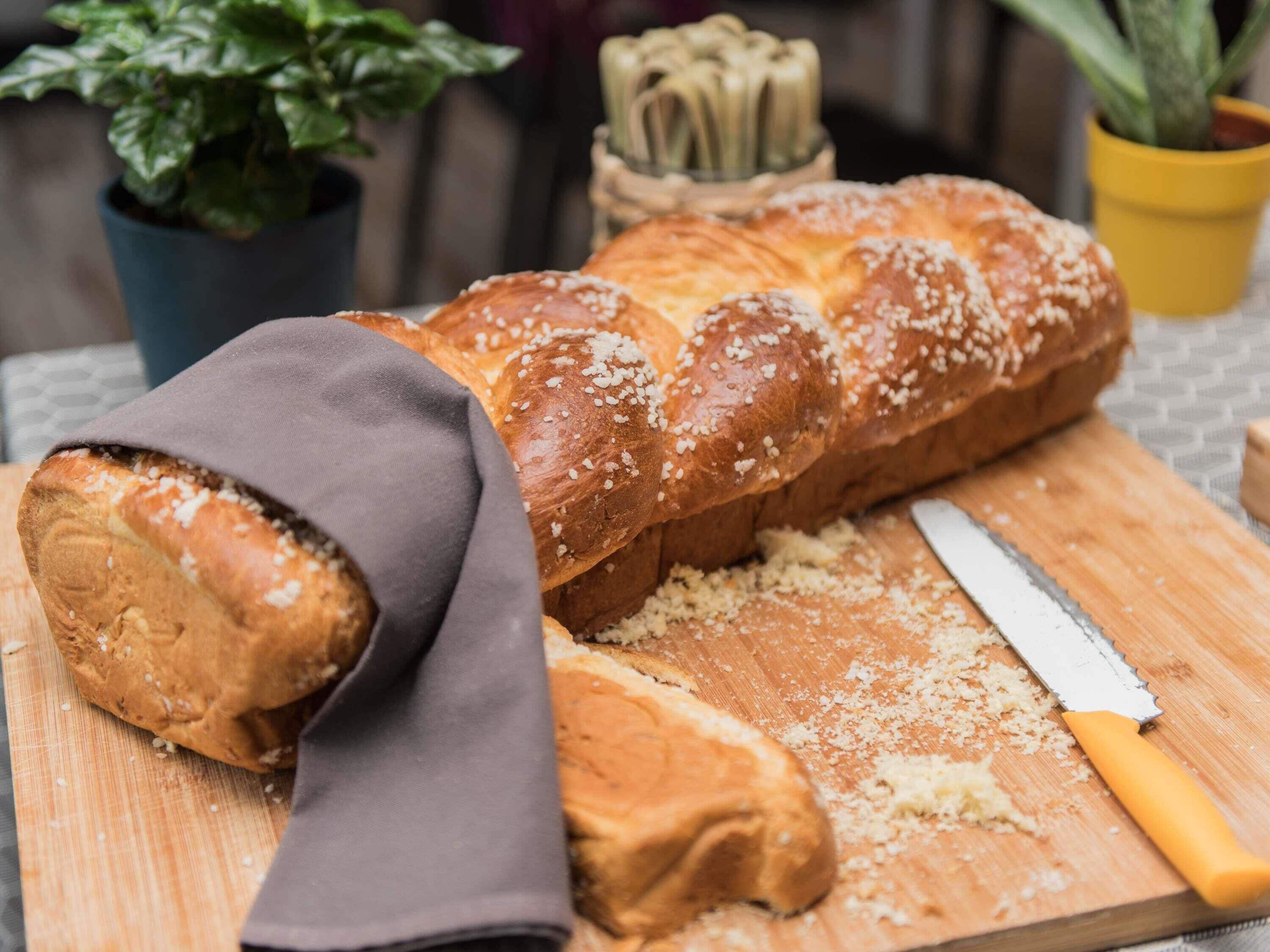 Une miche de pain sur une planche à découper en bois, avec un couteau, un torchon et une plante en pot en arrière-plan.