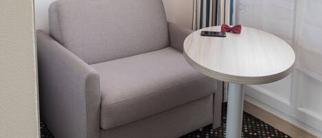 A hotel room with a grey sofa, a small round table with a red bow tie, a patterned carpet, and a blue accent wall.
