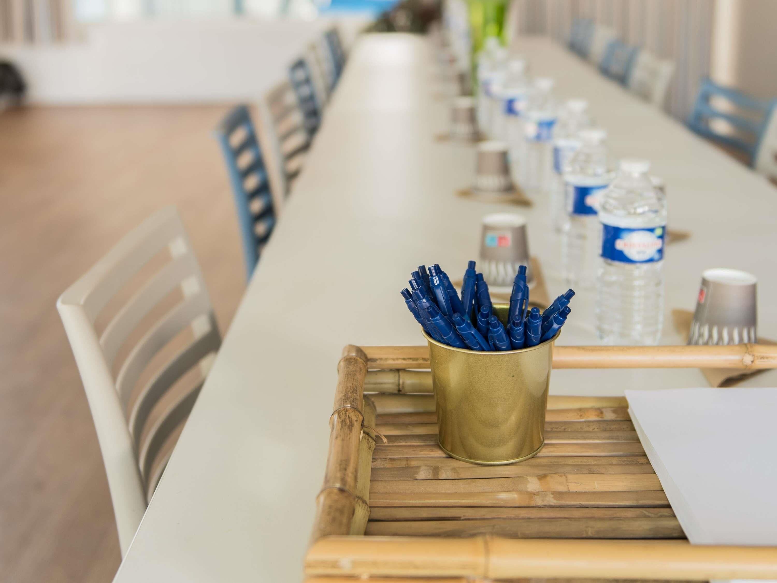 Una larga mesa de conferencias con sillas, una copa dorada con bolígrafos, botellas de agua y un atril para papeles.