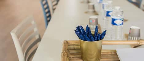 Una larga mesa de conferencias con sillas, una copa dorada con bolígrafos, botellas de agua y un atril para papeles.