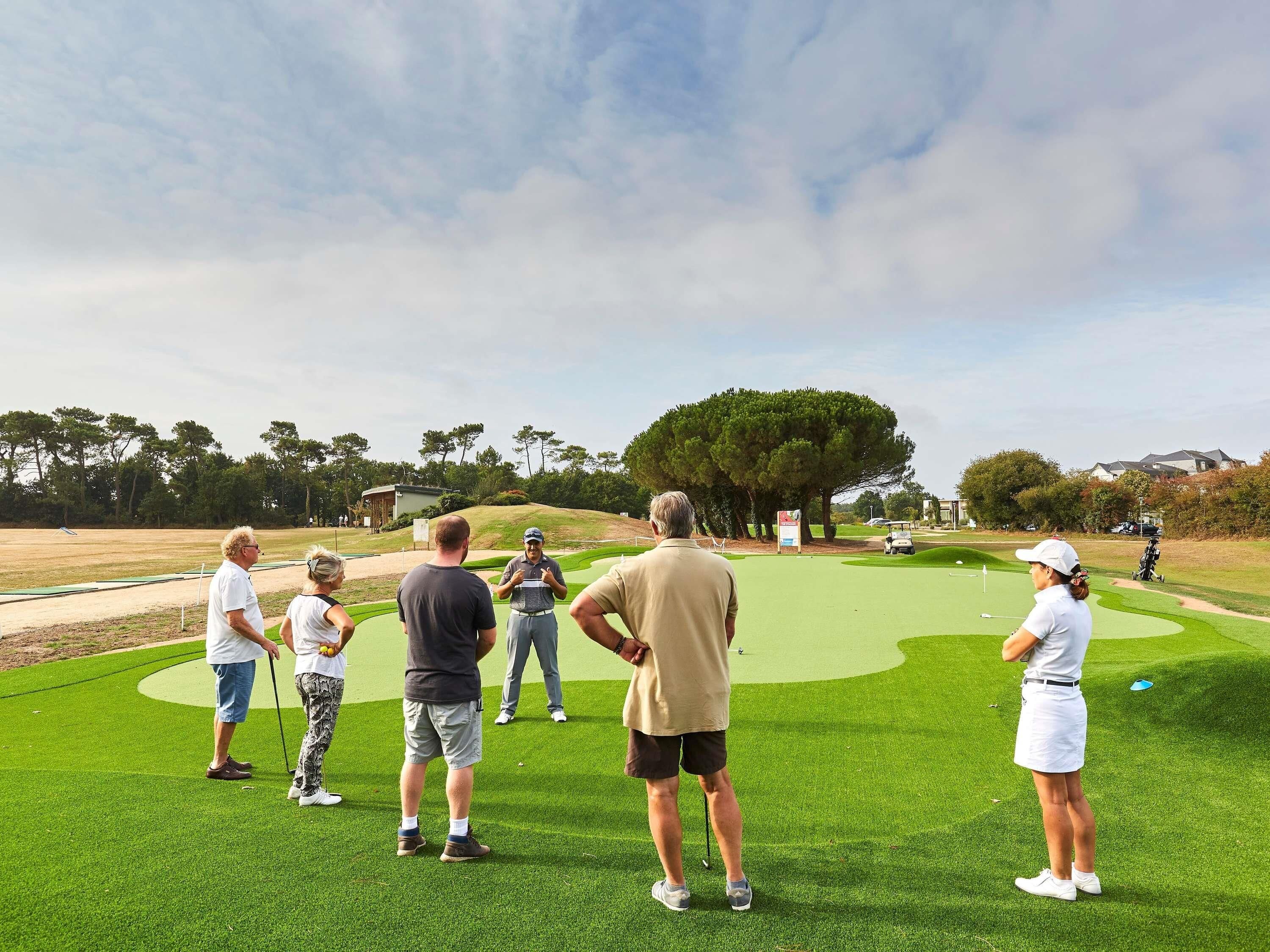 A golf course with players and spectators, surrounded by trees and a clear sky.