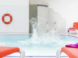 Une piscine avec une fontaine, une bouée de sauvetage et deux chaises longues orange.