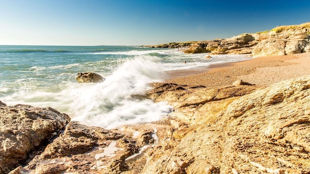 A rocky beach with waves crashing onto the shore, a clear sky, and distant cliffs. - ibis Styles Saint Gilles Croix de Vie (Saint-Gilles-Croix-de-Vie)