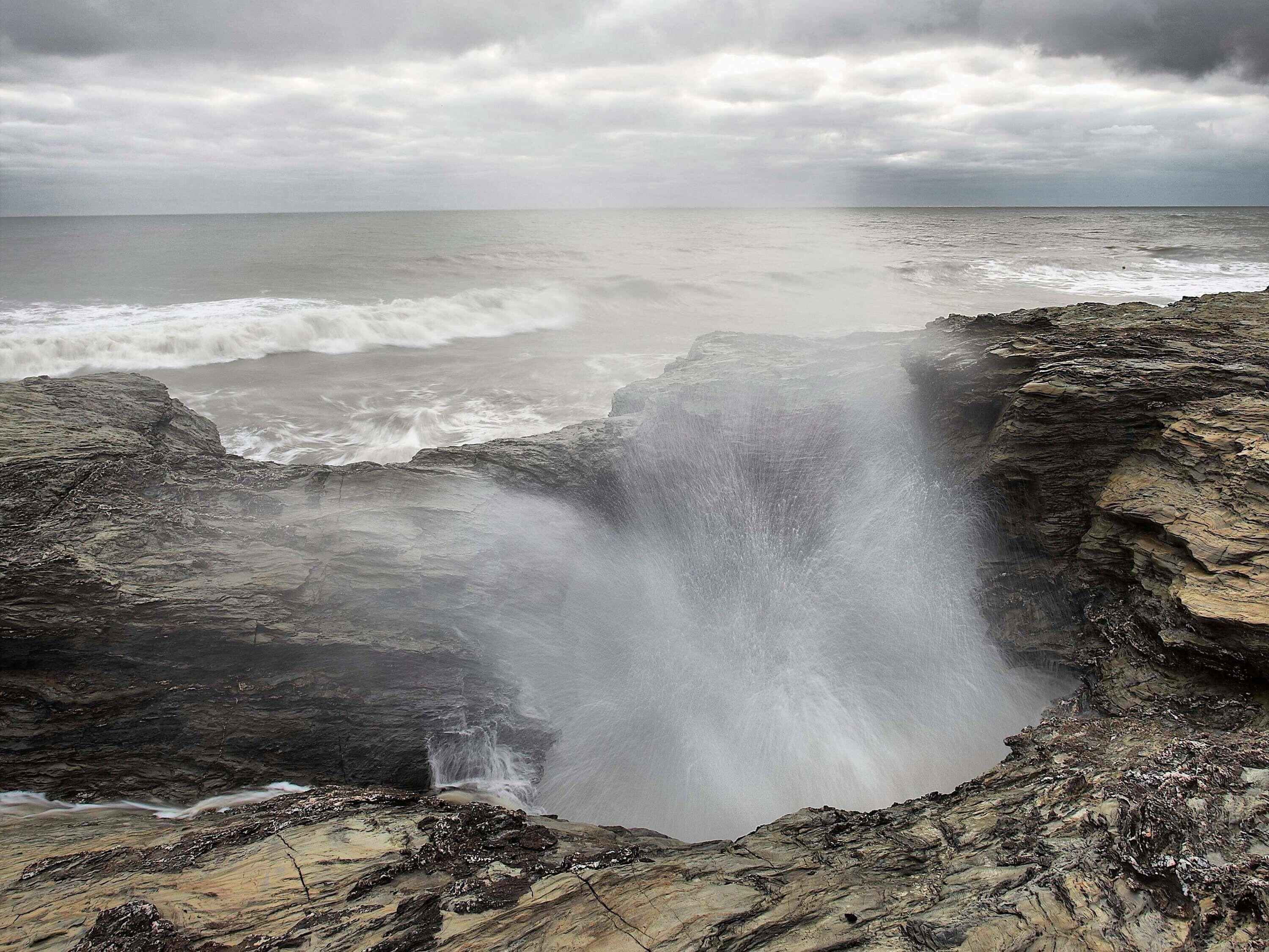 Un paysage côtier avec une cascade, un terrain rocheux et l’océan.