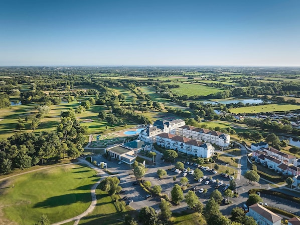 Vista aérea de un campo de golf con un club de campo, zona de estacionamiento y edificios residenciales.
