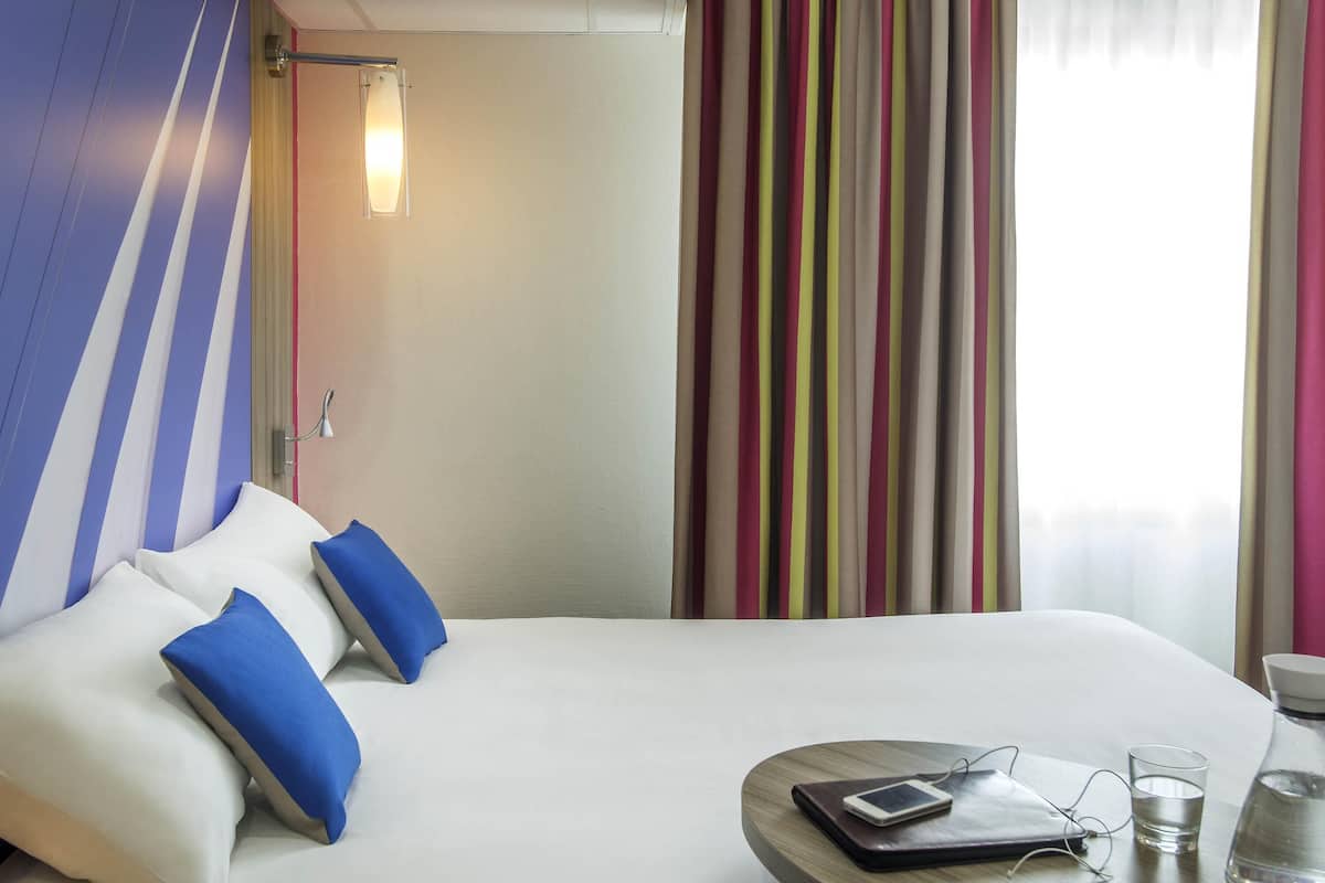 Une chambre d’hôtel avec un lit, des oreillers, une table de chevet avec un téléphone, des lunettes et une bouteille d’eau.