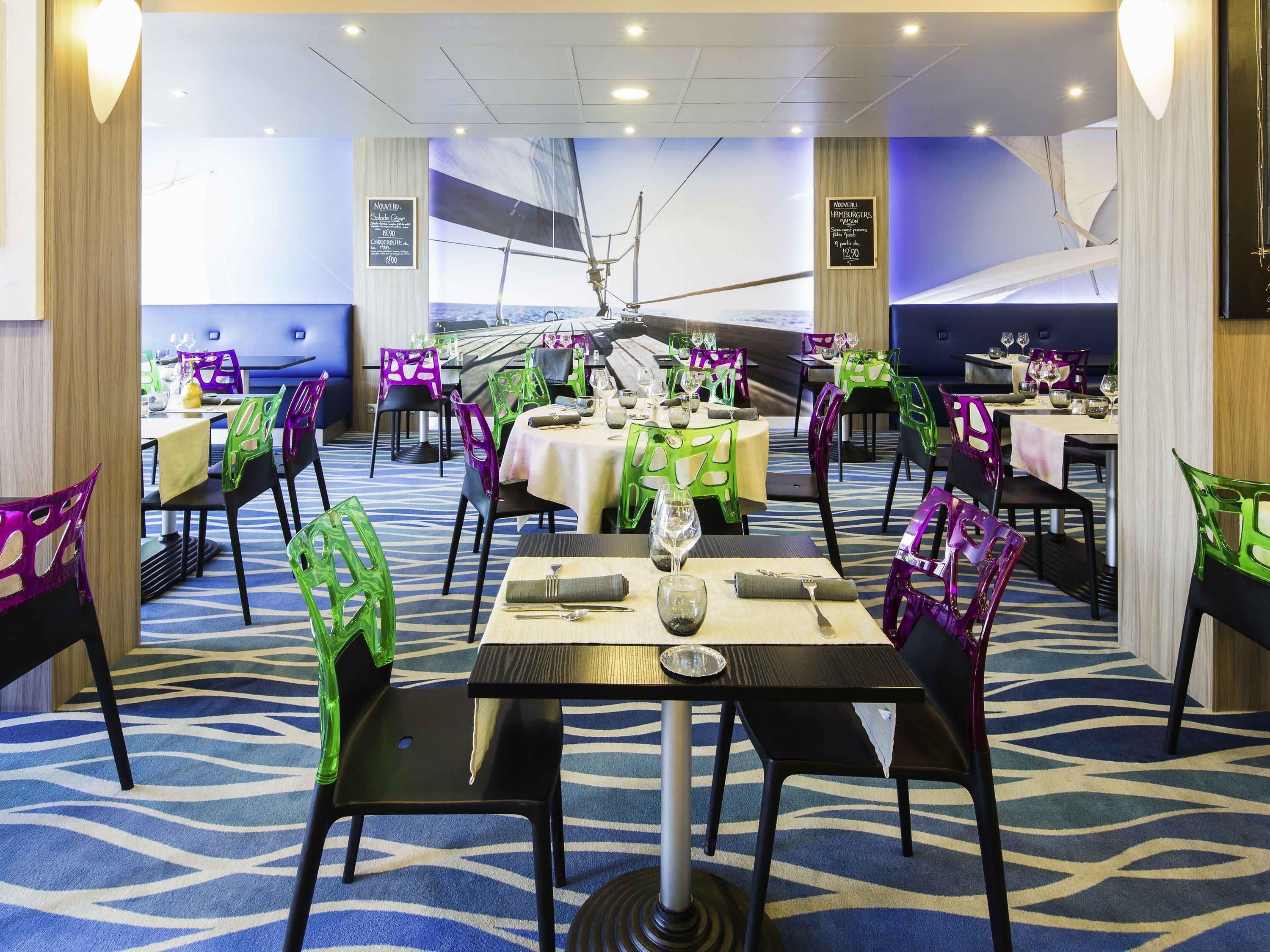 A restaurant with tables and chairs, a sailboat mural, and a blue carpet.