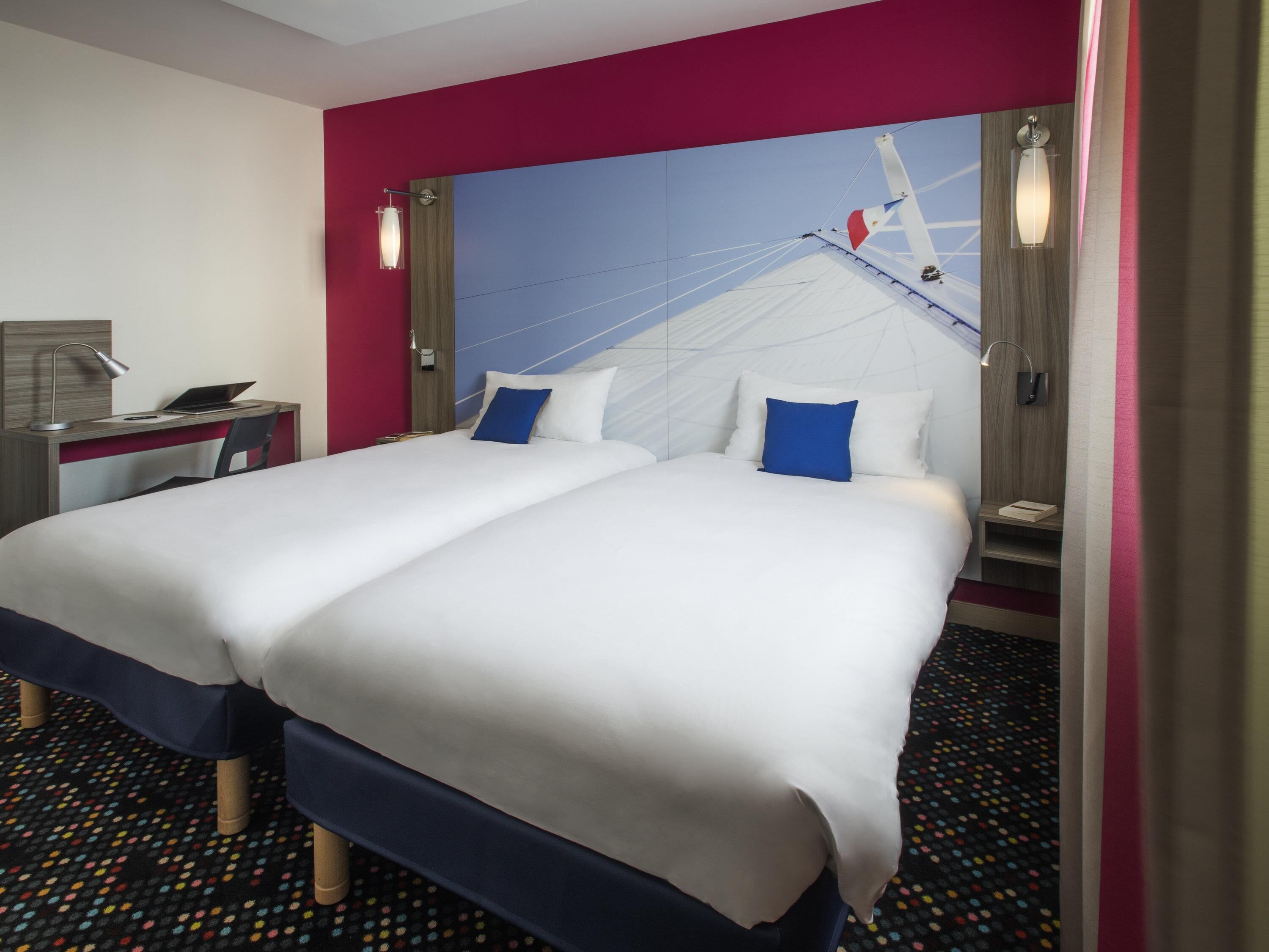 A hotel room with a large bed, a desk with a laptop, and a modern wall design.
