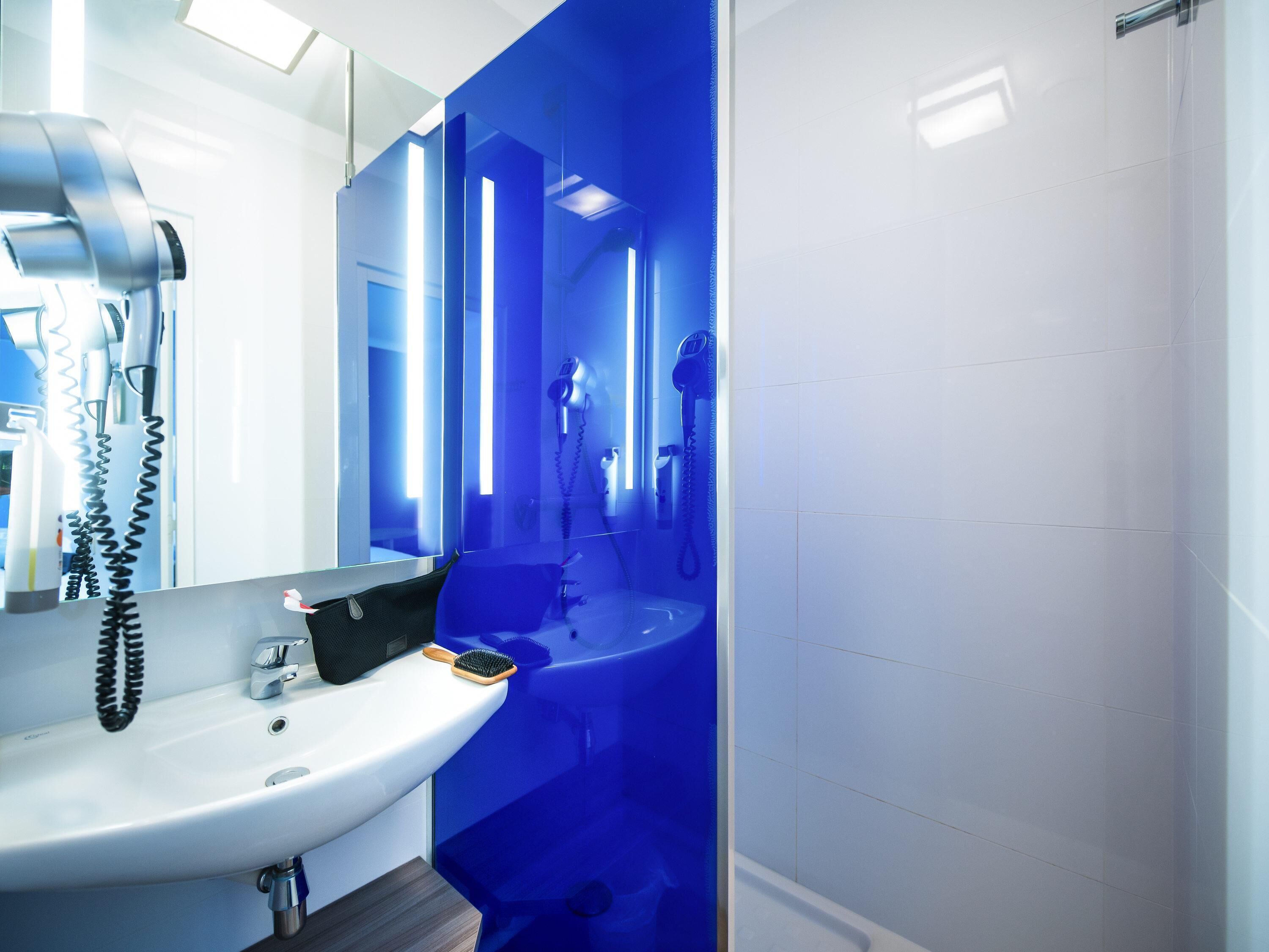 Ein modernes Badezimmer mit einem weißen Waschbecken, einem Föhn und einem Spiegel.