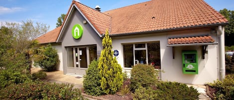 A building with a green logo, a tiled roof, and a small garden area.
