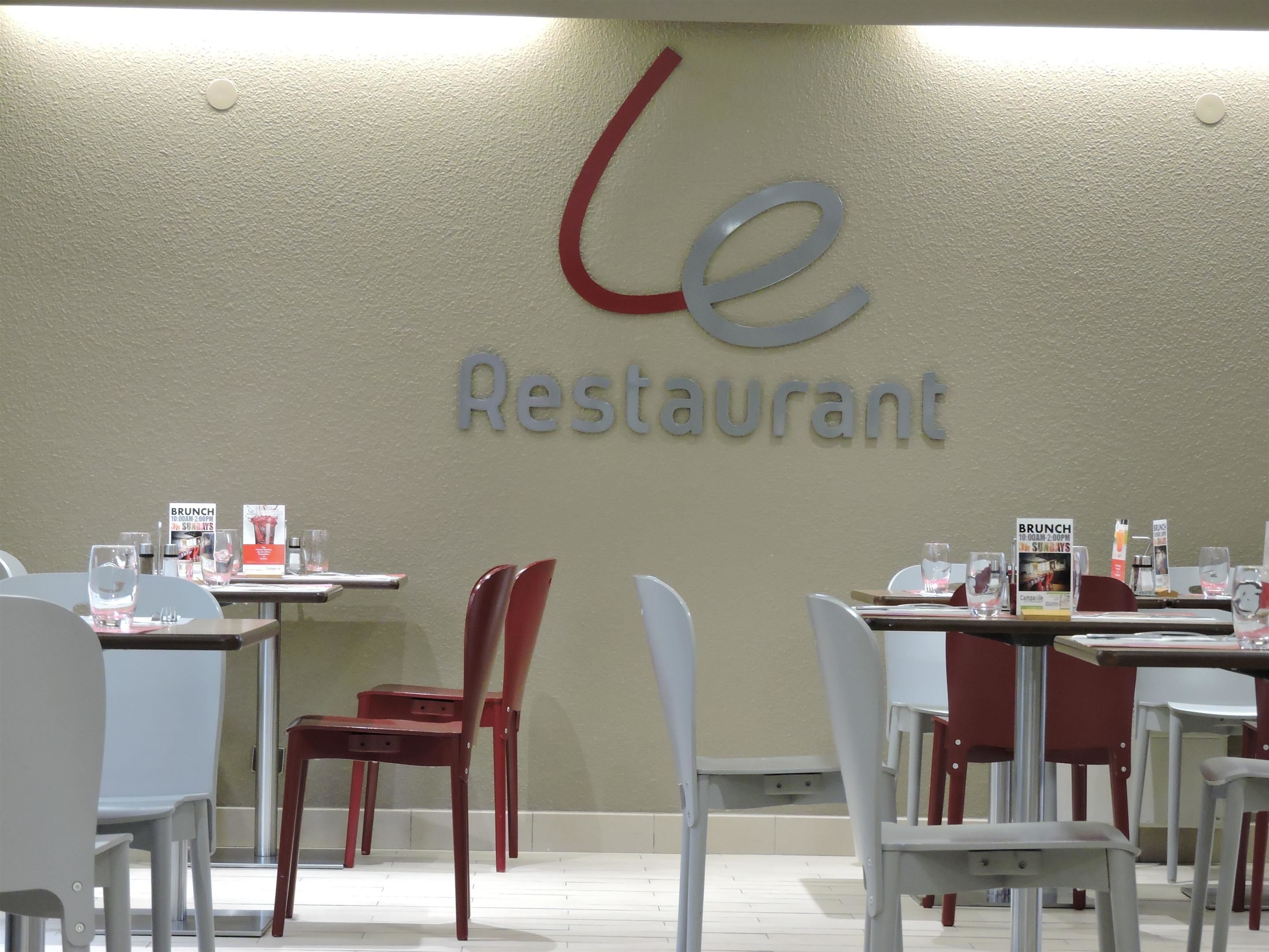 A restaurant interior with tables, chairs, and a wall sign reading "Le Restaurant".