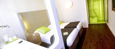 A compact hotel room with a bed, bedside table, and a small seating area.