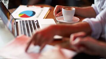 Een laptop, een taartdiagram en een kop koffie op een tafel.