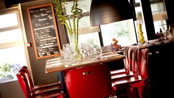 A restaurant interior with a wooden table set for dining, red chairs, a menu board, and a plant in a glass vase.