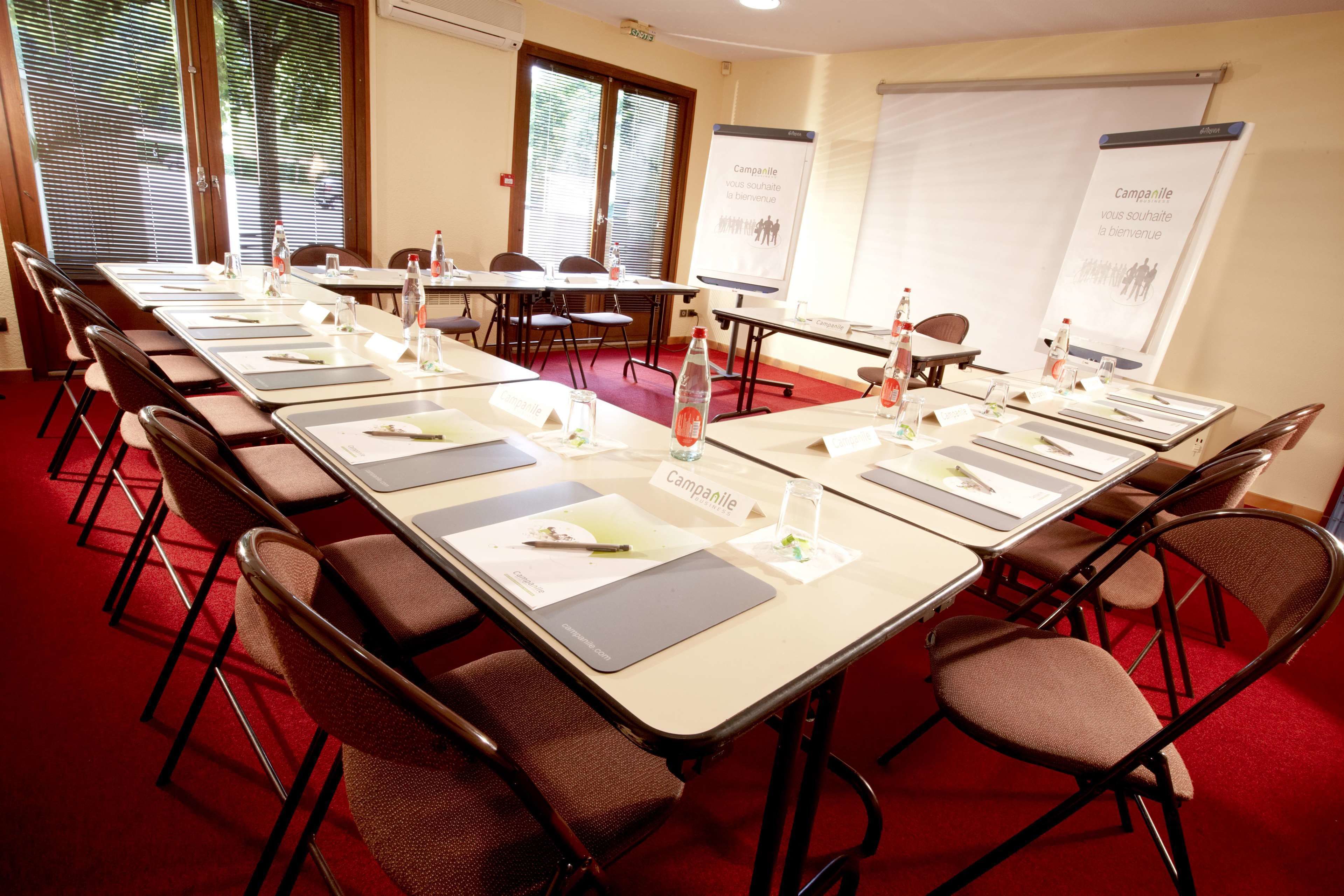 A conference room with a long table, chairs, name cards, and presentation screens.