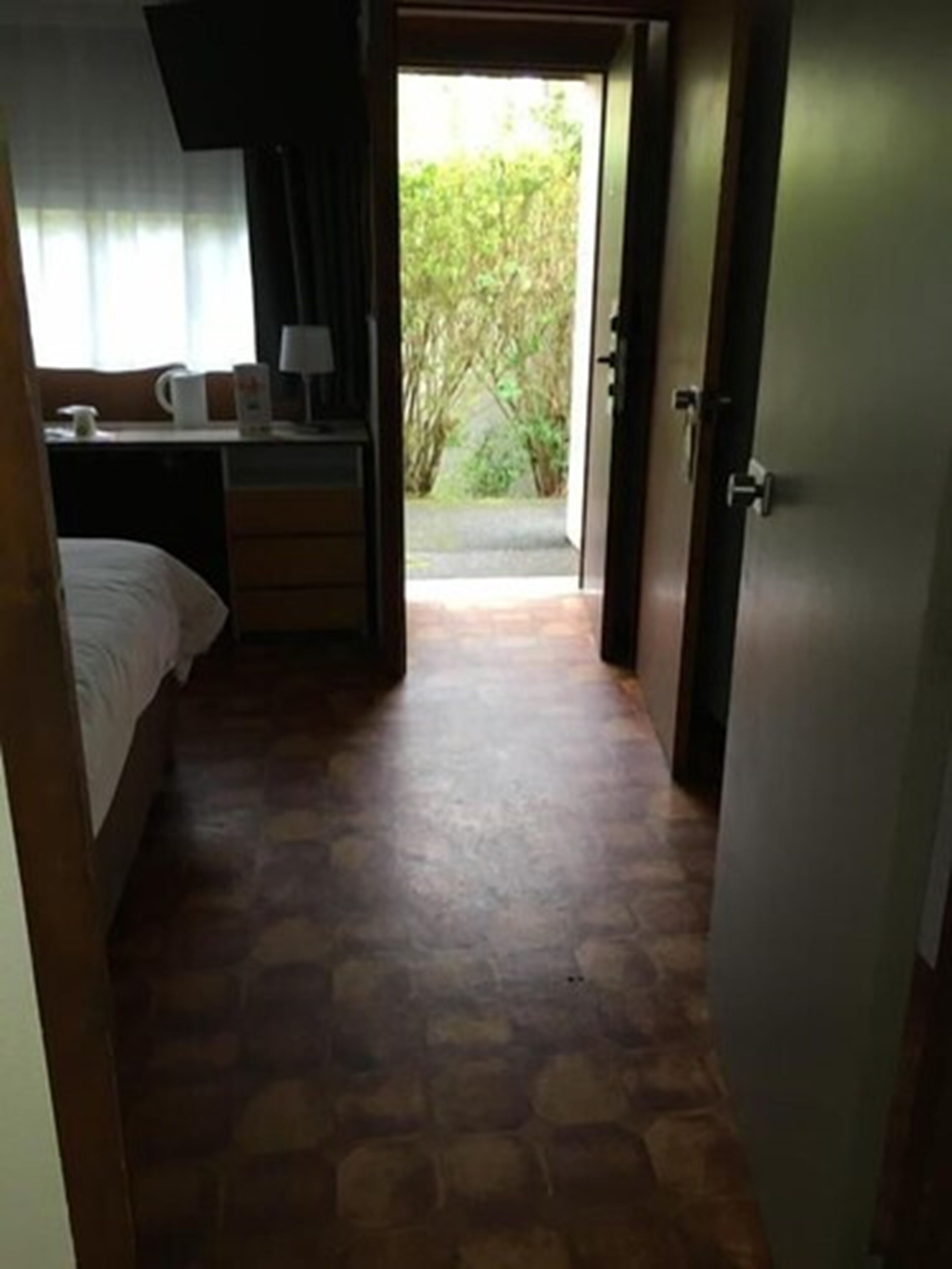 A bedroom with a bed, a desk, and a chair. There is a window with curtains, and a door leading outside.