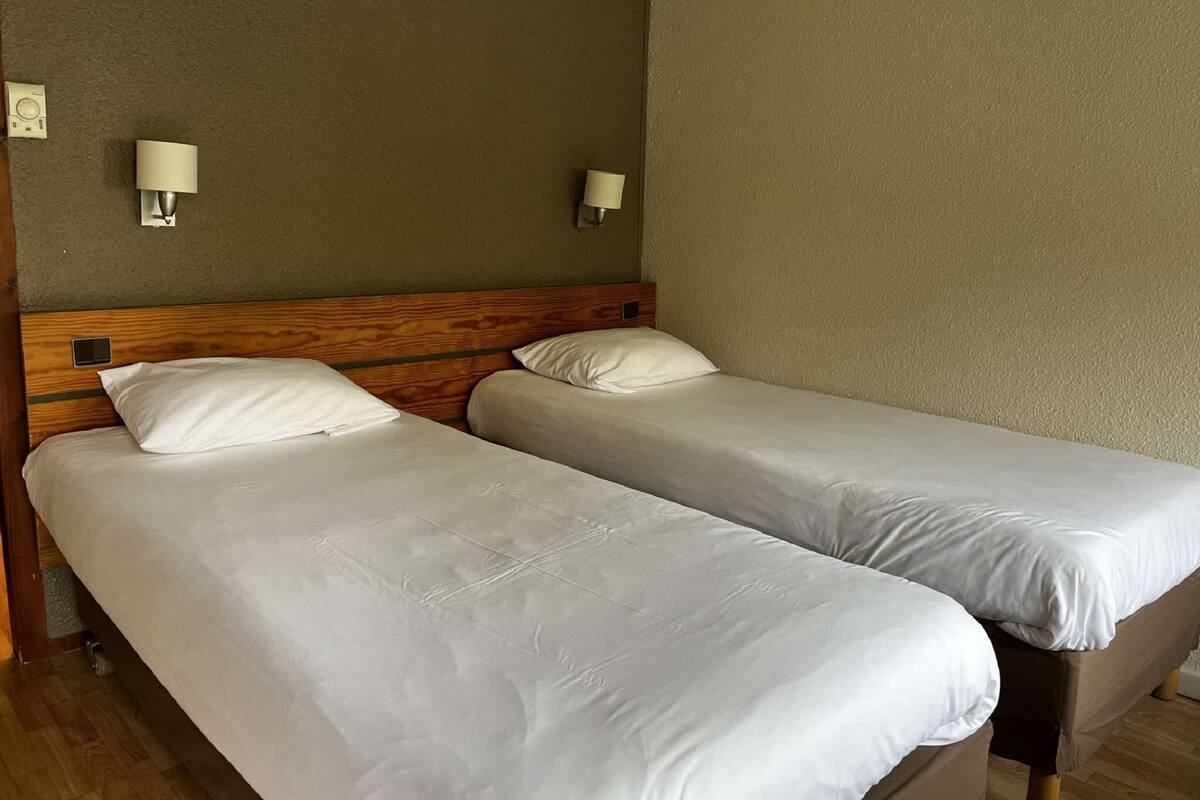 Habitación de hotel con dos camas individuales, cabeceros de madera y lámparas de pared.