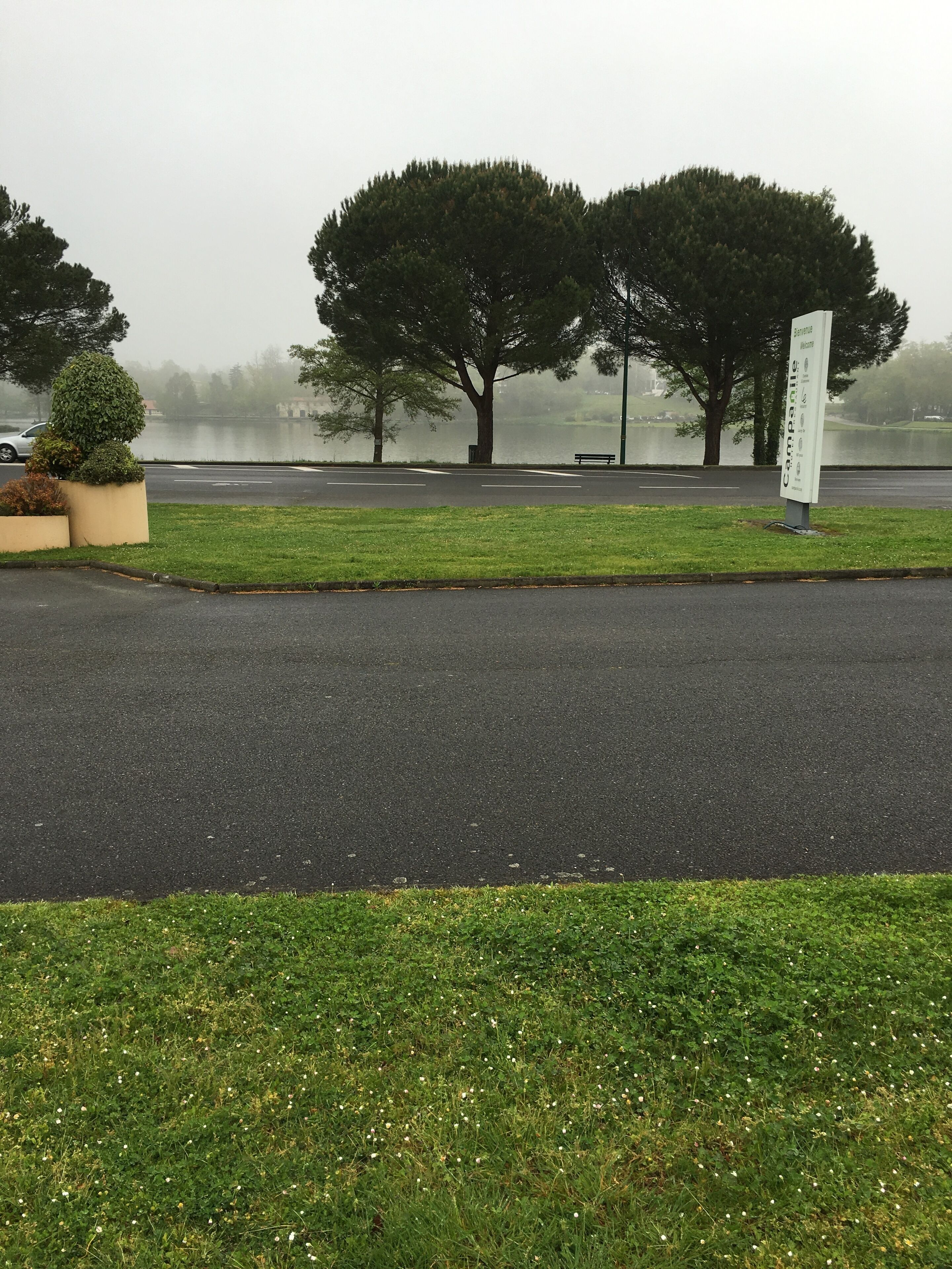 A parking lot with a sign, trees, and a body of water in the background.