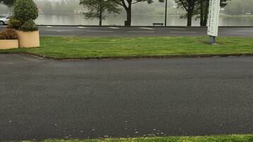A parking lot with a sign, trees, and a body of water in the background.