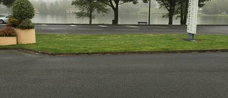 A parking lot with a sign, trees, and a body of water in the background.