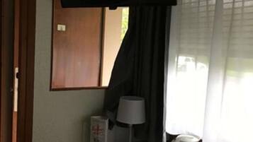 A hotel room with a bed, a bedside table with a lamp, a window with curtains, and a view of the outside.