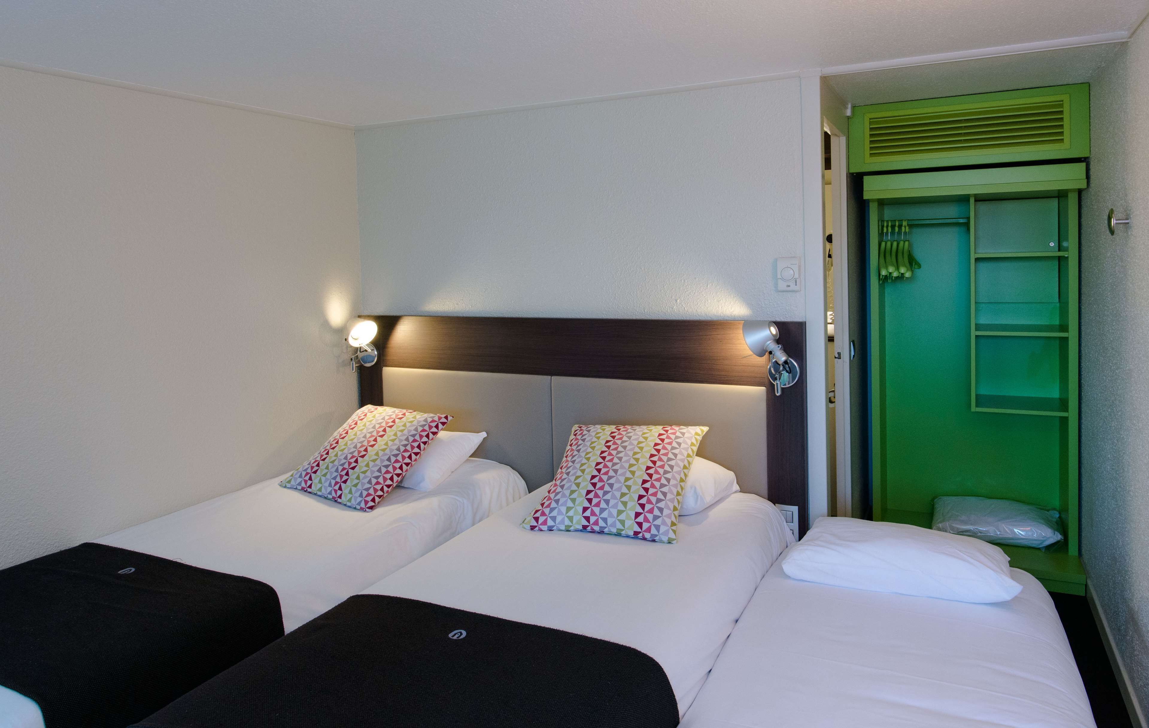Een hotelkamer met twee bedden, elk voorzien van een kussen met een kleurrijk geometrisch patroon, een donker hoofdbord en een groene deur.