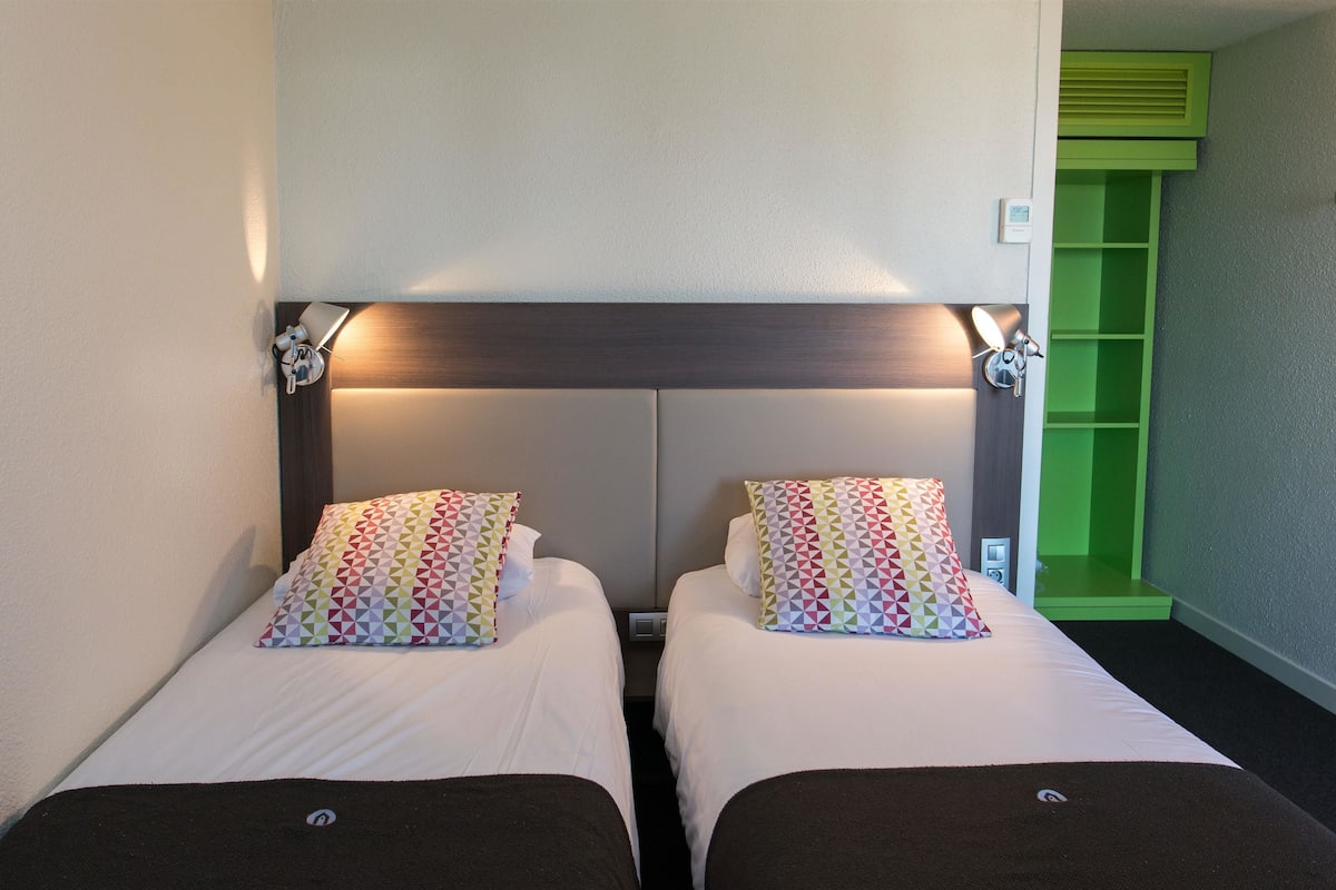 Une chambre d’hôtel avec deux lits, chacun doté d’un oreiller à motifs et d’une tête de lit avec éclairage intégré.