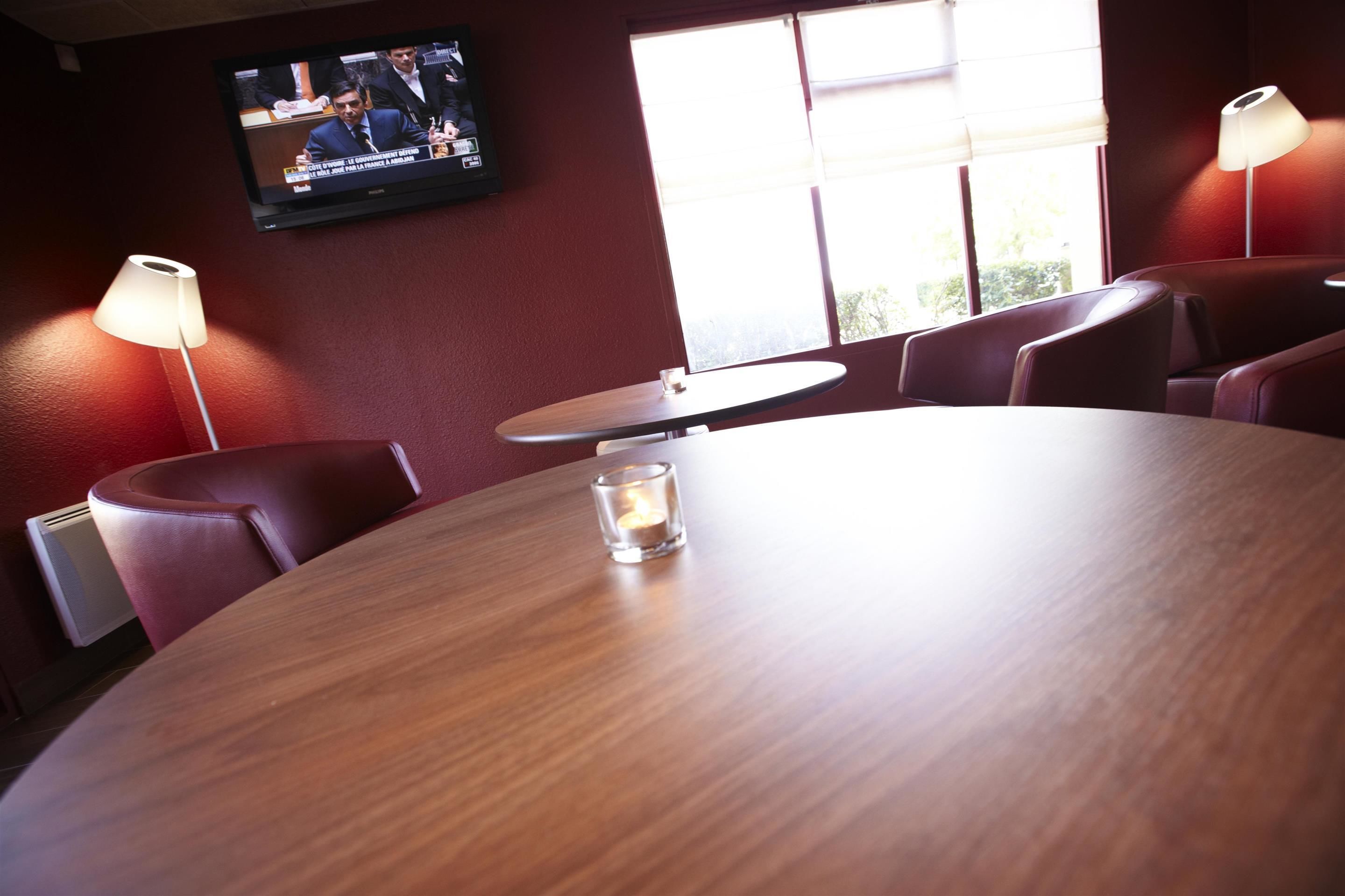 A conference room with a round table, two chairs, a TV on the wall, and a window with blinds.