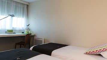 Habitación de hotel con dos camas, un escritorio con silla, una lámpara y una ventana con cortinas.