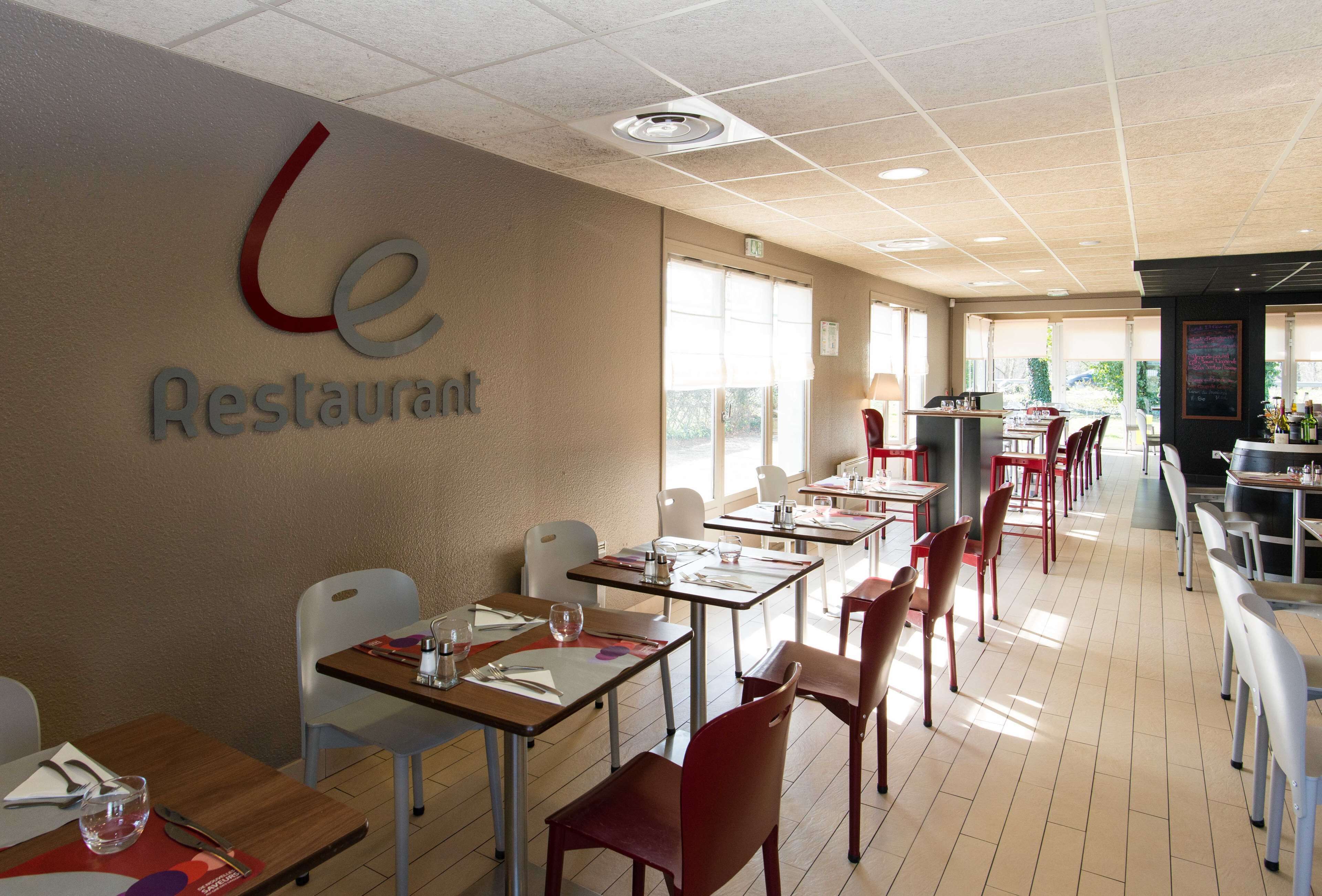 Un interior de restaurante con mesas y sillas, un letrero en la pared y vistas a través de las ventanas.
