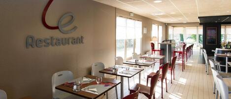 A restaurant interior with tables and chairs, a sign on the wall, and a view through the windows.