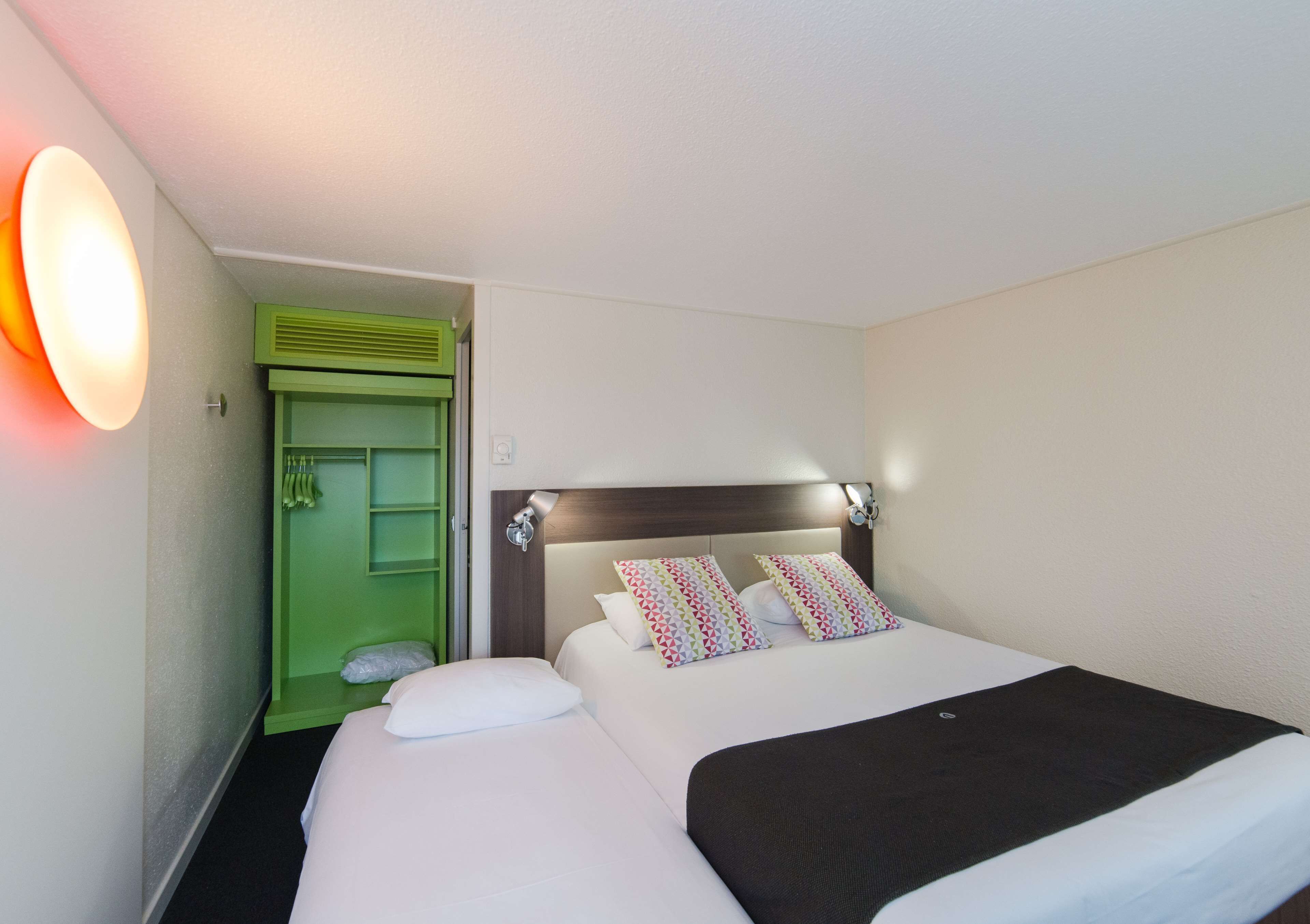 Una habitación de hotel con una cama, un armario verde y una lámpara fijada a la pared.
