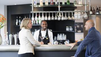 Uma área de bar com um bartender, um cliente e um balcão.