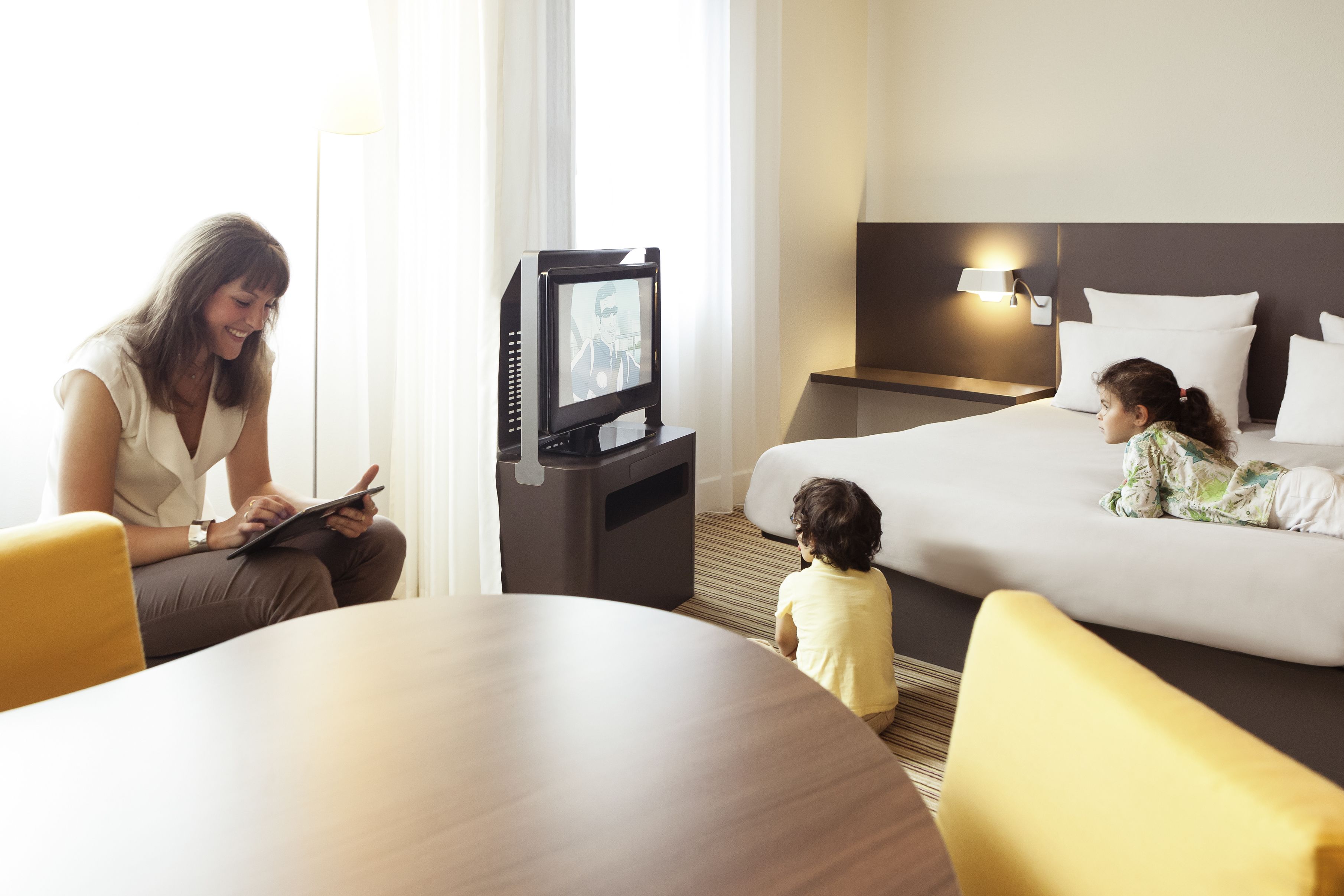 Habitación de hotel con cama, mesita de noche con televisor, mesa con sillas y ventana con cortinas.