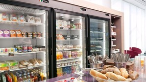 Un área de desayuno autoservicio con refrigeradores llenos de bebidas, aperitivos y pan.
