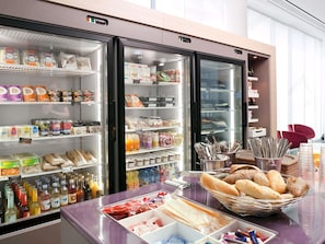 Un espace de petit-déjeuner en libre-service, équipé de réfrigérateurs remplis de boissons, de collations et de pain.