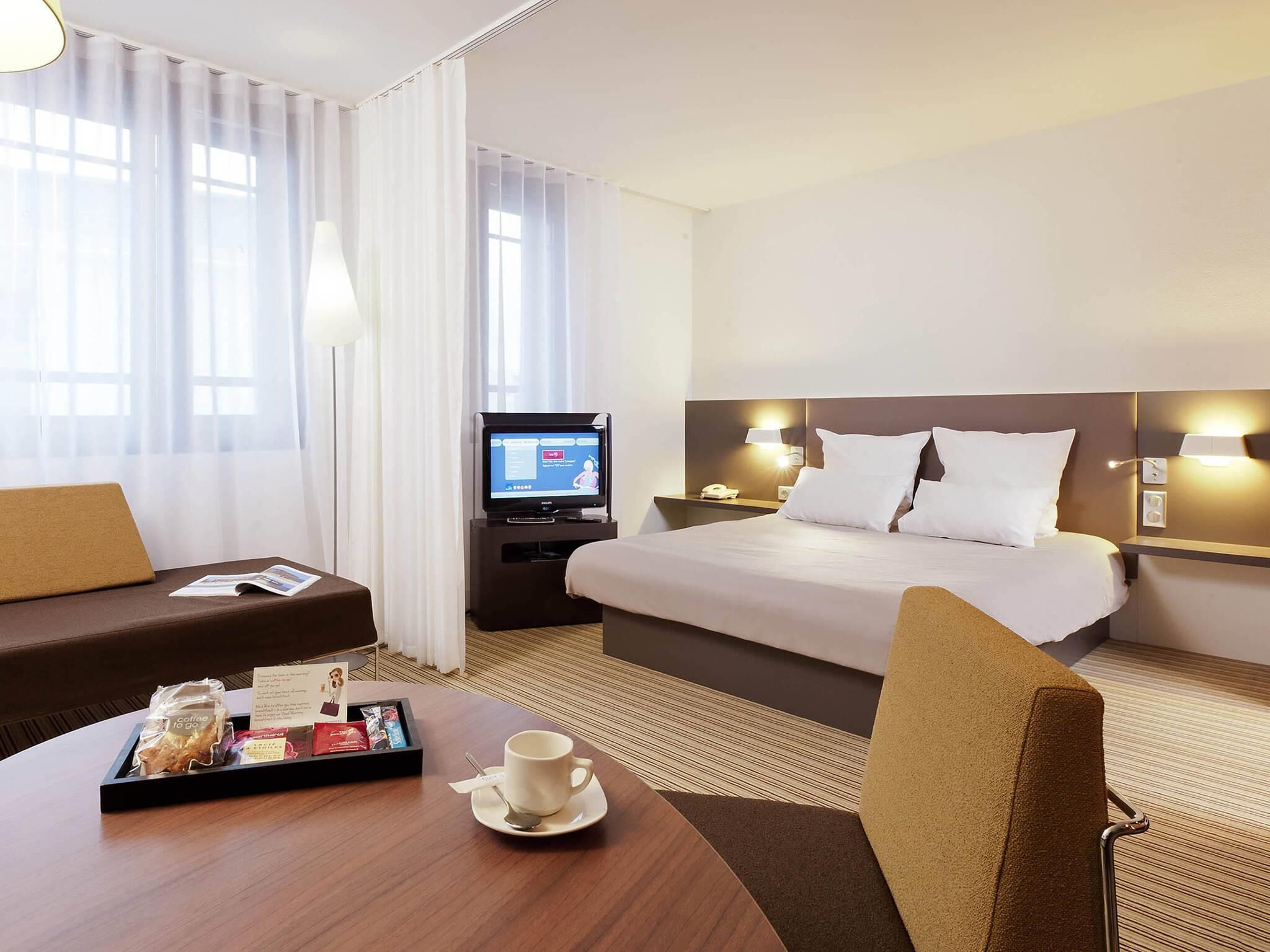 A hotel room with a bed, a desk with a coffee tray, a TV, and a sofa.