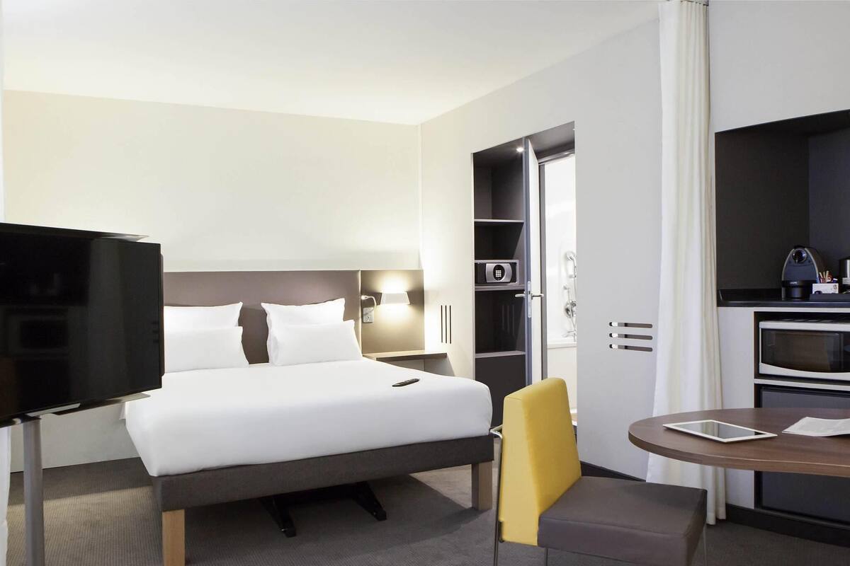 Une chambre d’hôtel comprenant un lit, une télévision, un bureau avec une chaise et une kitchenette.