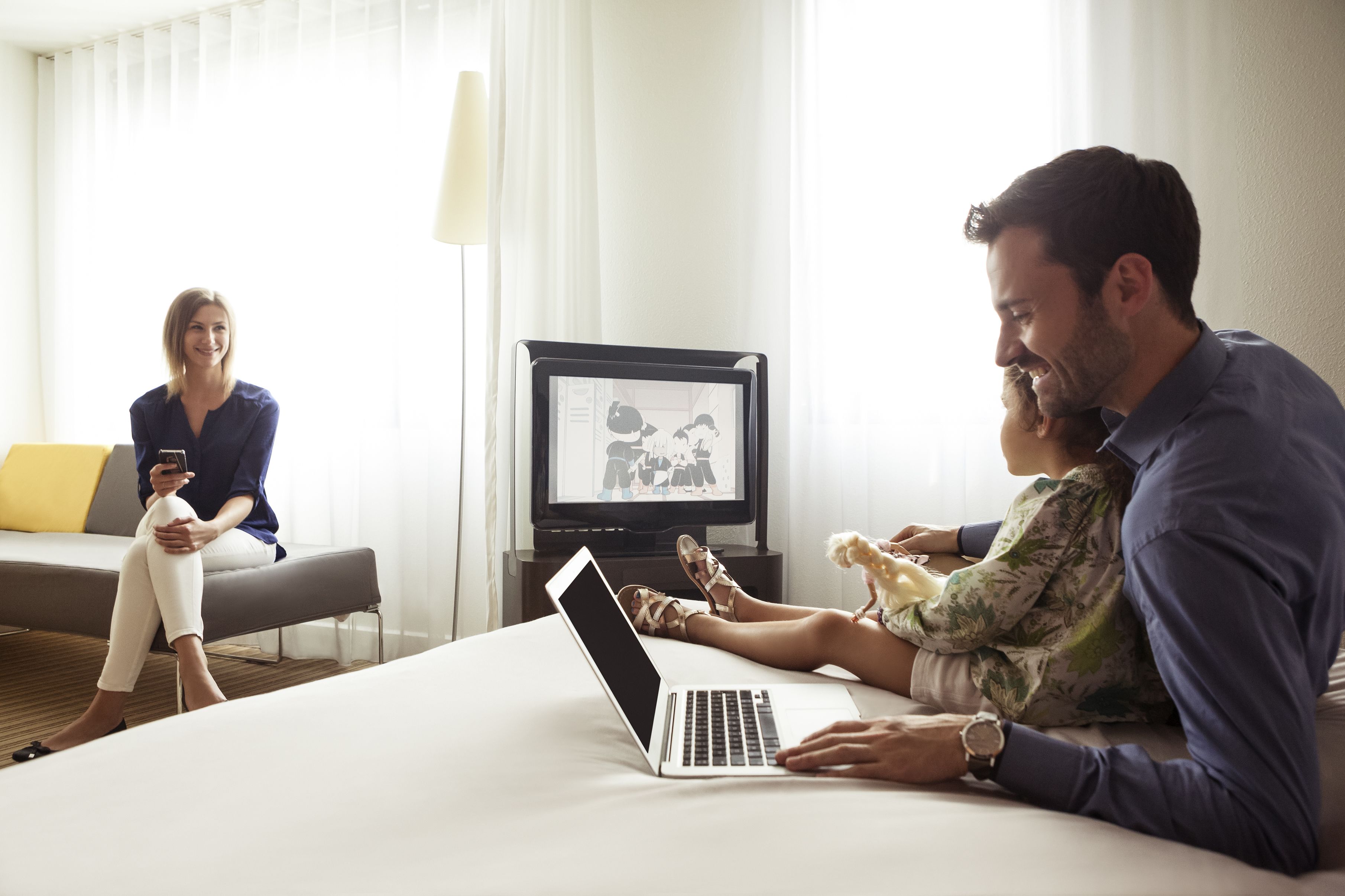 Ein Hotelzimmer mit einem Bett, einem Laptop, einem Fernseher und einer Person, die einen kleinen Hund hält.