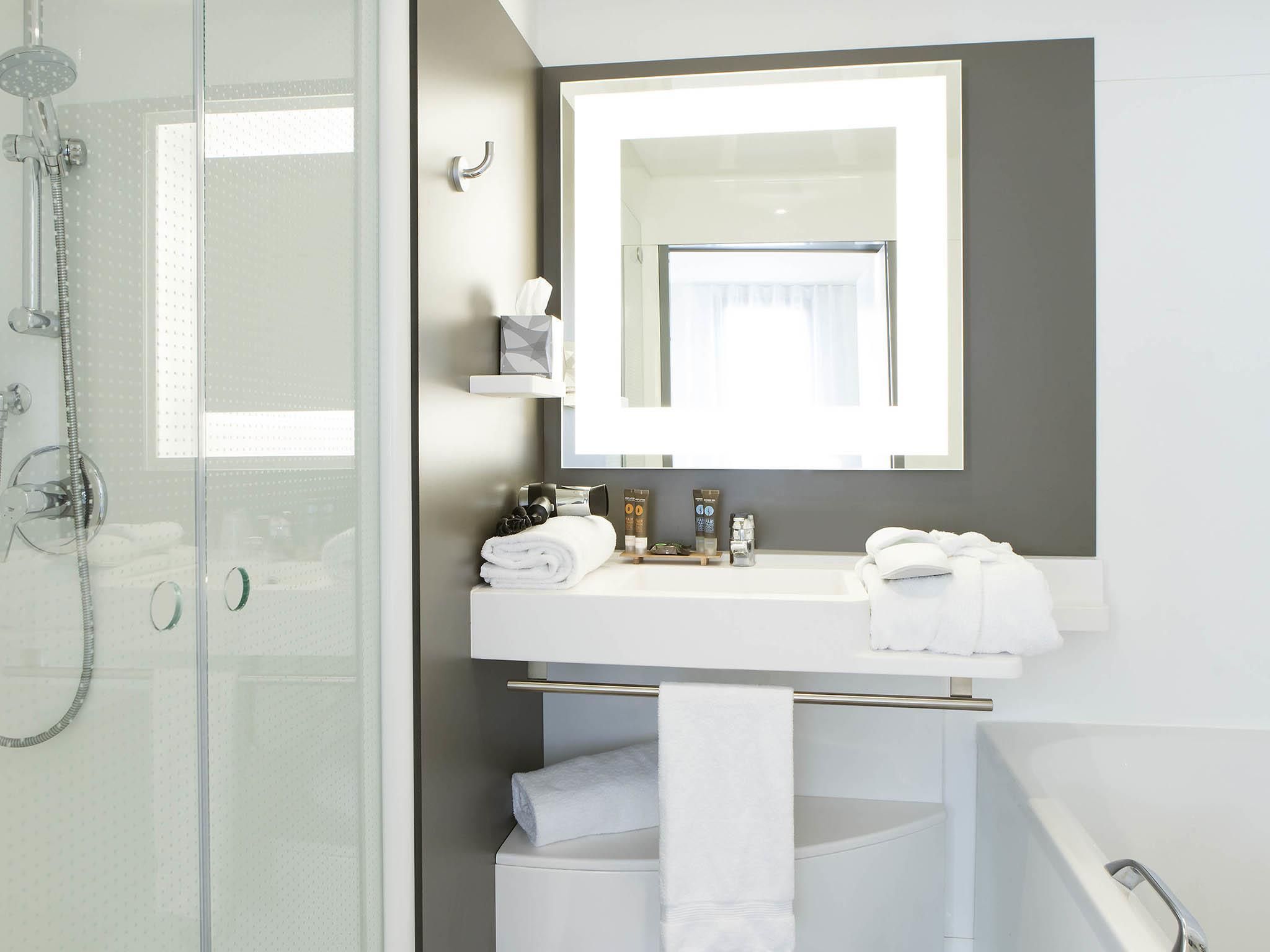 A modern bathroom with a glass shower enclosure, a white sink with a mirror above it, and a towel rack.
