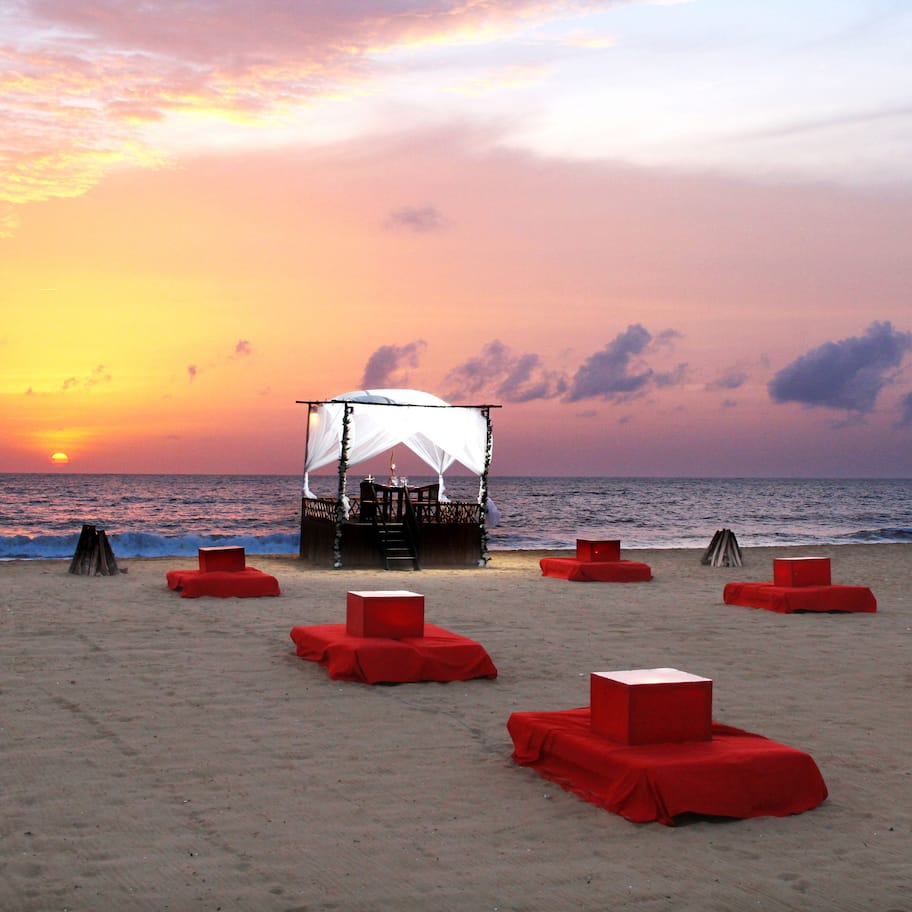 A beach with red lounge chairs and a covered area with a white canopy.