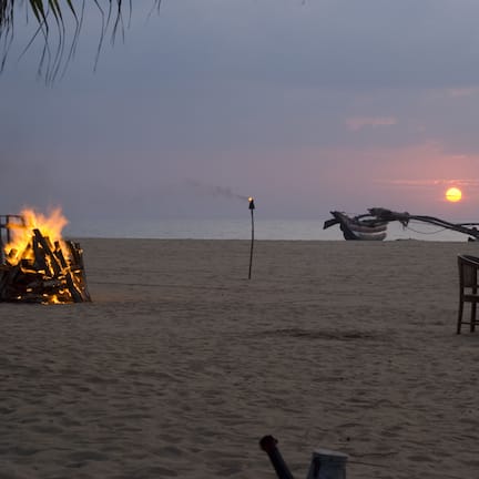 A beach scene with a fire, a table with chairs, and a sunset in the background.