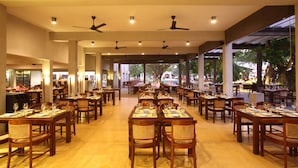 A spacious restaurant with multiple dining tables and chairs, ceiling fans, and a view of the outdoors. - Jetwing Beach (Negombo)