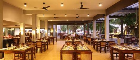 A spacious restaurant with multiple dining tables and chairs, ceiling fans, and a view of the outdoors.