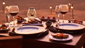 A table set for a meal with wine glasses, plates, and a candle, overlooking a beach at sunset. - Jetwing Beach (Negombo)