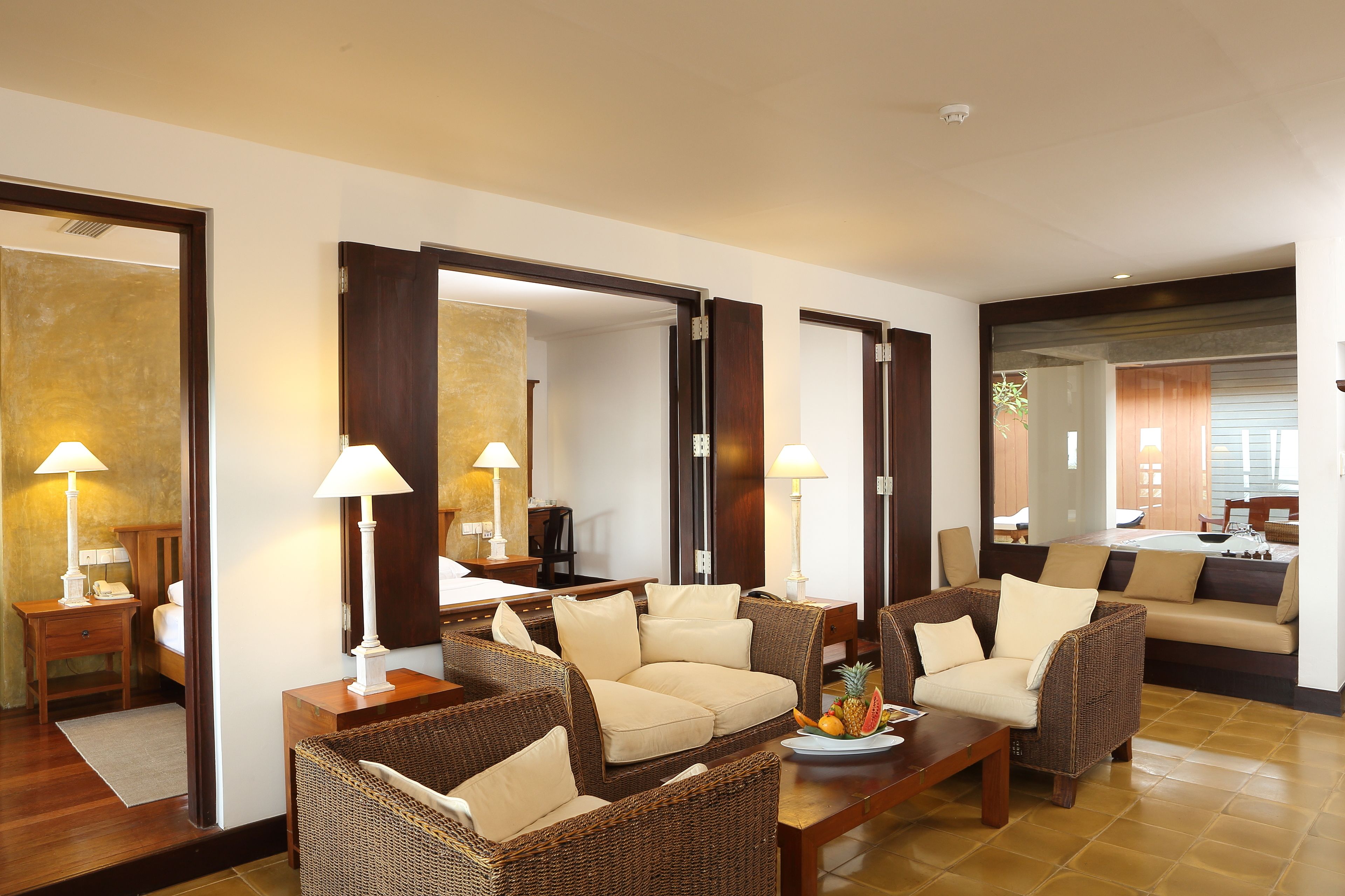 A spacious living area with wicker furniture, a coffee table with fruit, and a large mirror reflecting the room.
