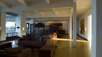 A spacious living area with a large sofa, ottomans, and a floor lamp. There are large windows and a view of the outdoors.