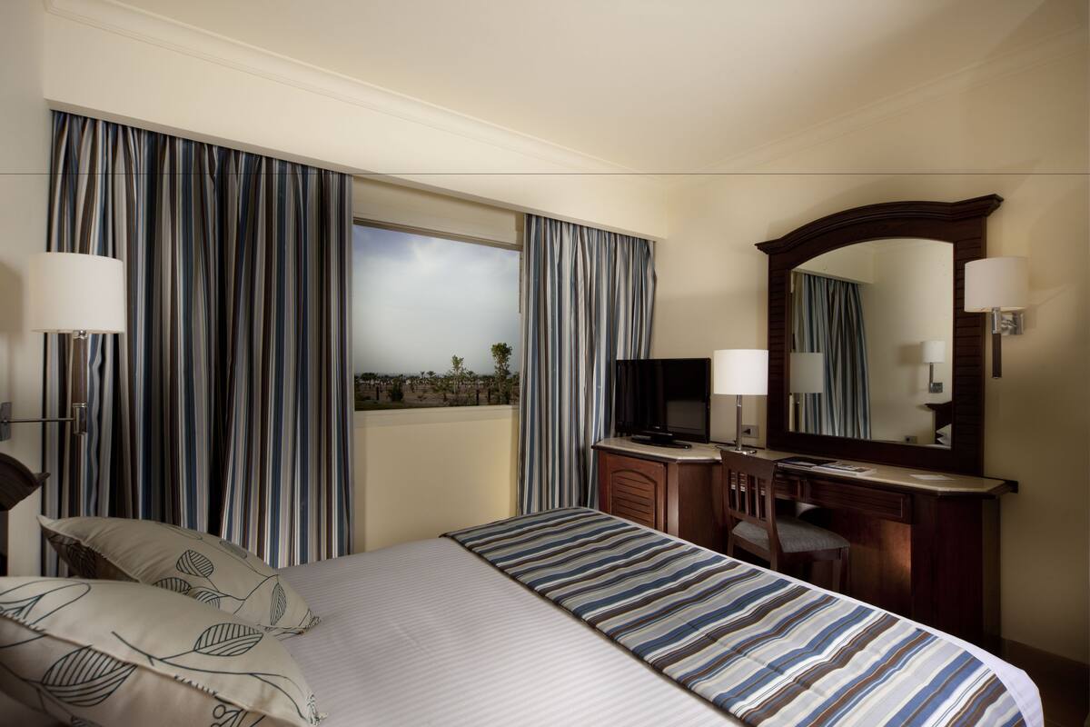 A hotel room with a bed, a desk with a computer, a mirror, and curtains.